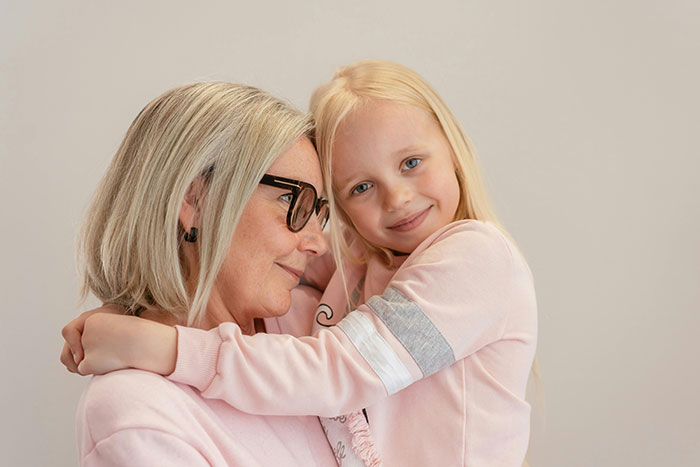 Grandmother hugging her granddaughter, both wearing pink sweaters, reflecting a close family bond despite recent tensions.