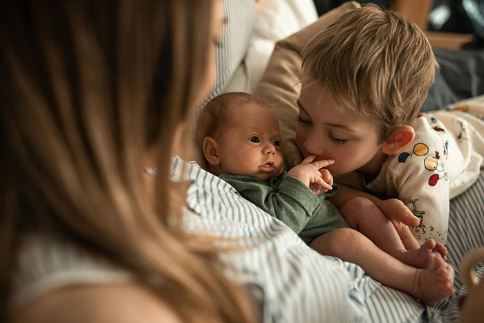 Mother holding baby with young sibling nearby, highlighting family tension dynamics.