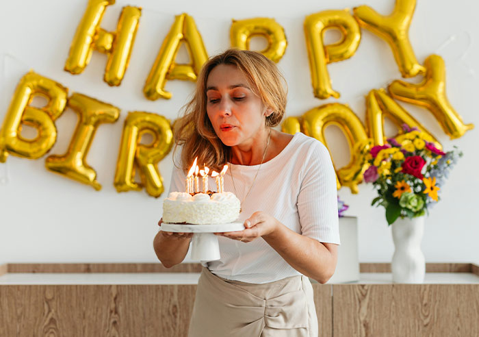 Woman blowing out candles on a birthday cake in front of golden "Happy Birthday" balloons, highlighting toxic family dynamics.