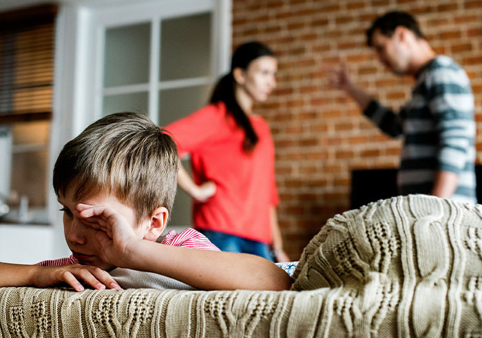 Child looking upset while parents argue in the background, highlighting a toxic family environment.