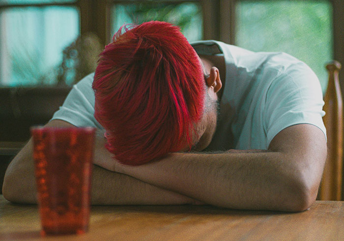 Person with red hair resting head on arms at a wooden table, highlighting toxic family dynamics.