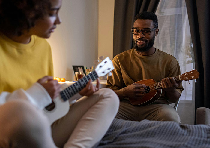 Two people playing ukuleles in a cozy room, highlighting family dynamics.