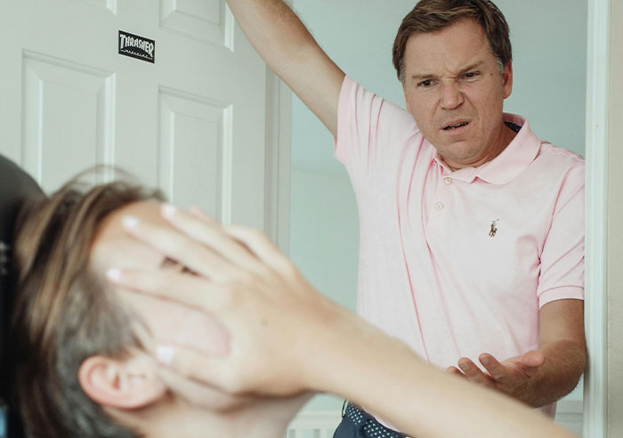 Man in pink shirt looking upset while talking to a person covering their face, illustrating a toxic family interaction.