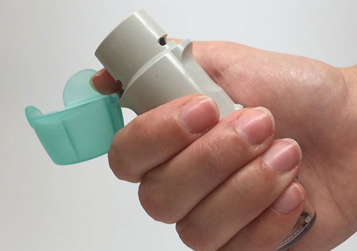 Hand holding an inhaler with a green cap, representing toxic family impact.