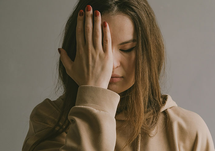 Woman in a beige hoodie covering her face, depicting emotion related to toxic family dynamics.