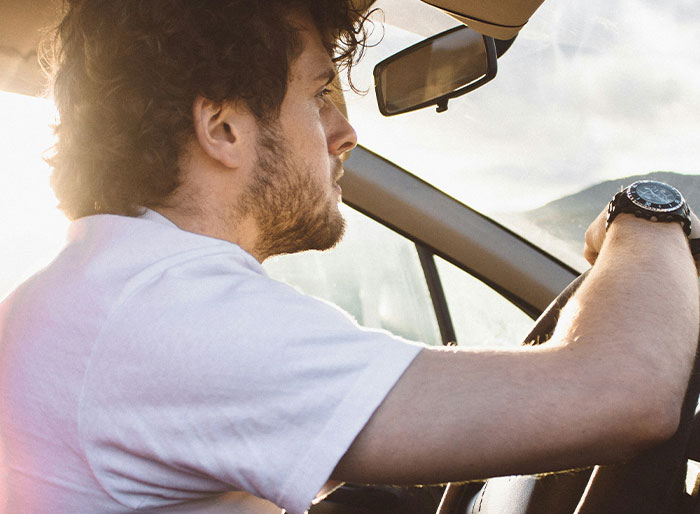 A person in a white shirt driving a car, reflecting on a toxic family experience during sunset.