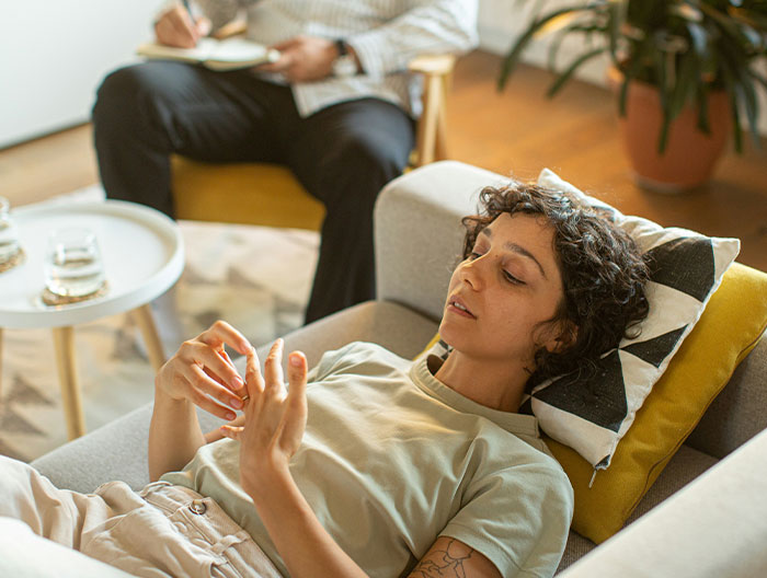 Person lying on a sofa in a therapy session discussing toxic family issues, with a therapist taking notes in the background.