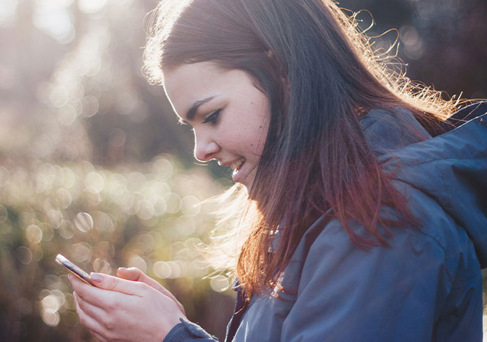 Young woman in a park using her phone, capturing a moment of family tension and toxicity.