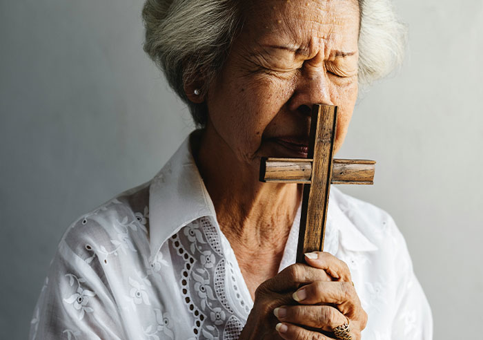 Elderly woman holding a cross, symbolizing faith amidst family toxicity challenges.