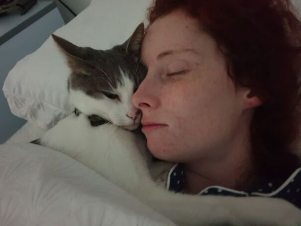 Woman sleeping with tucked kitten cuddled close on a bed.