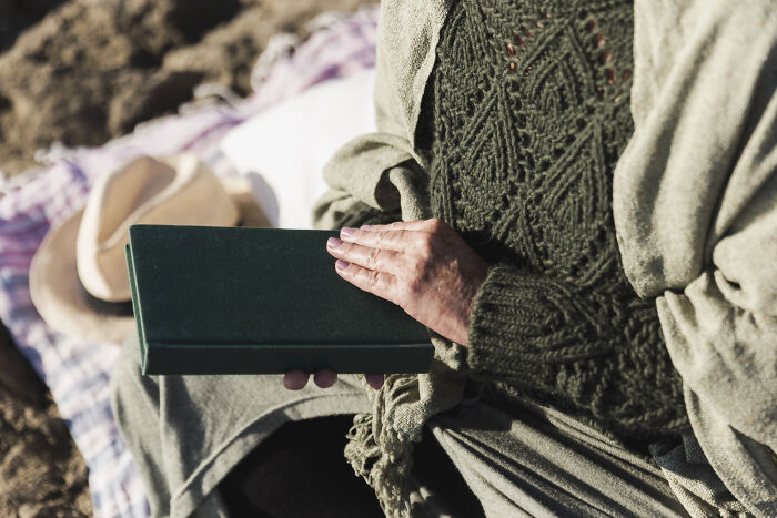 Person holding a green book on a blanket.