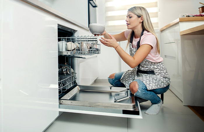 Woman loading a dishwasher incorrectly, with a bowl on the top rack, demonstrating using things the wrong way.