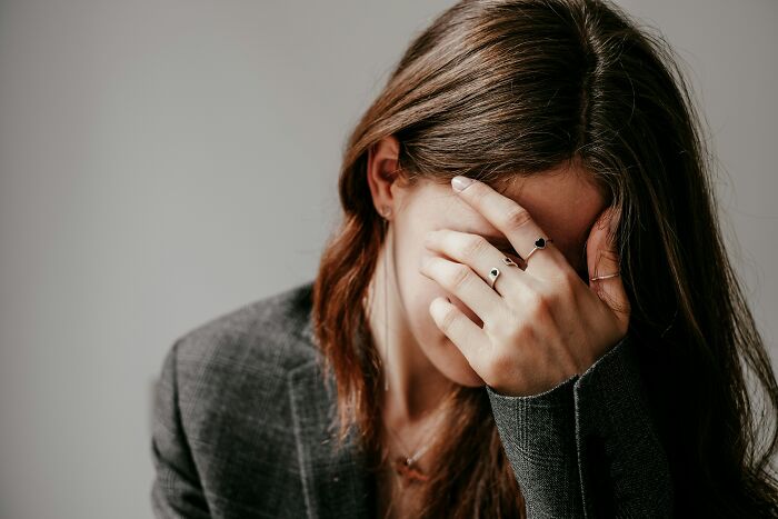 A woman in a blazer, holding her head in her hands, possibly concealing secrets from her loved one.