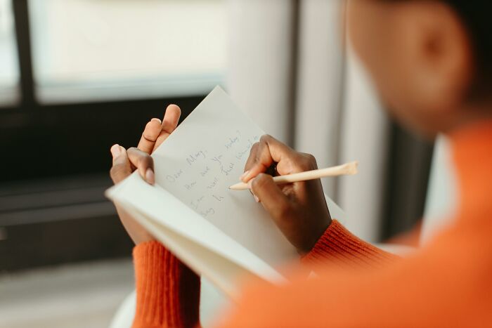 Person writes in a notebook, seated by a window, depicting vegan family concerns over neighbors cooking meat.