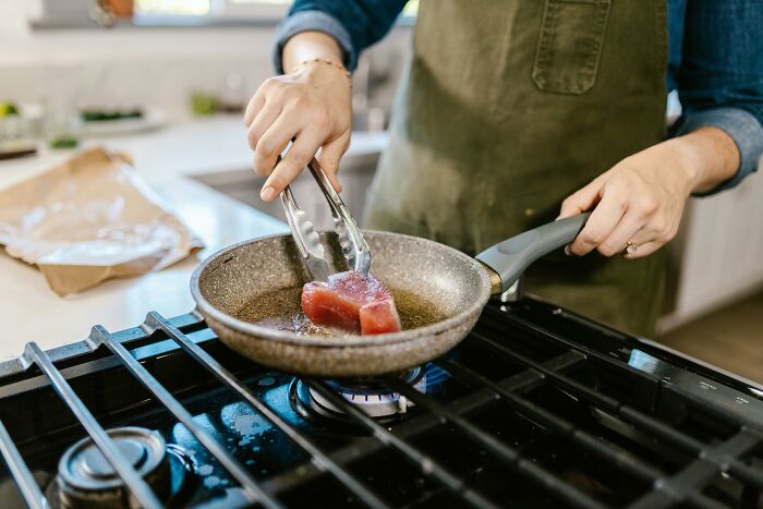 Person cooking meat in a pan on the stove, sparking drama with vegan neighbors.