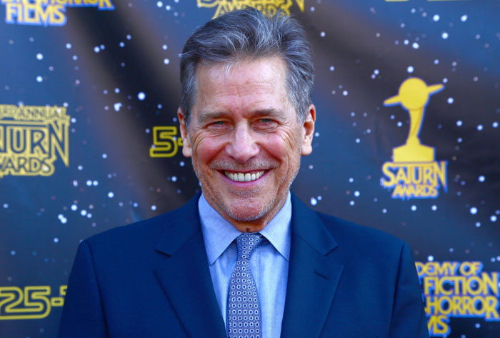 Man in a suit smiling at the Saturn Awards backdrop, representing Virgin River cast member.