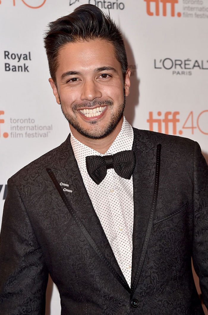 A smiling cast member of Virgin River at a red carpet event in a black suit and bow tie.