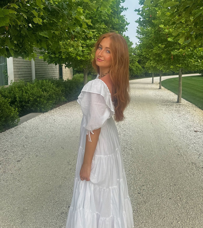 Peyton Spaht in white dress standing on a tree-lined path.