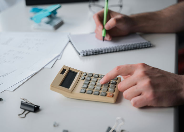 Person using a calculator and writing in a notebook, solving a mystery.