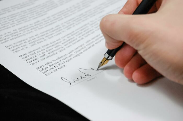 Hand signing a document with a pen, illustrating elements of costly items.