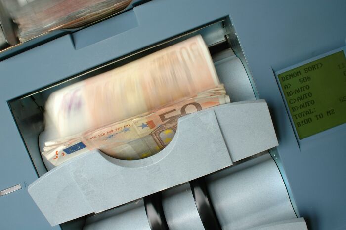 Euro banknotes being counted in a machine, highlighting wasteful expenses.