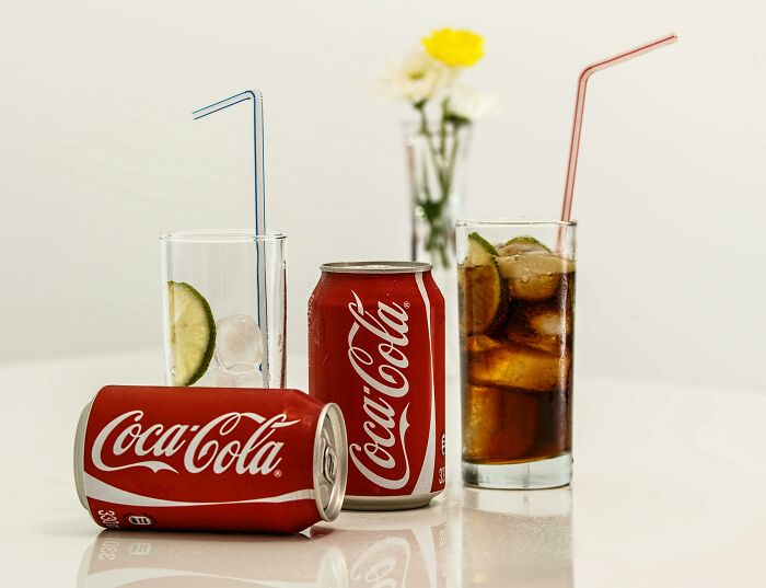 Coca-Cola cans and glasses on a table with a flower vase in the background.