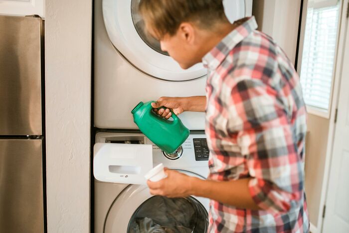 Person using fabric softener, pouring from green bottle into a washing machine compartment.