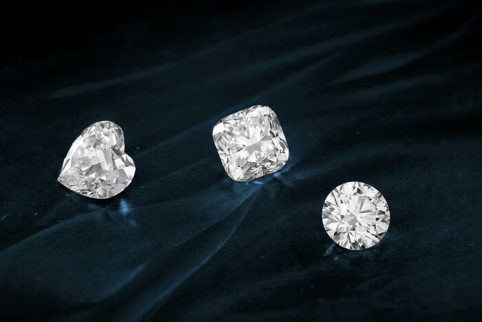 Three sparkling diamonds sit on a dark velvet fabric, representing luxury and extravagance.