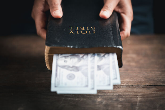 Hands holding a Bible with dollar bills inside, symbolizing unexpected costs.