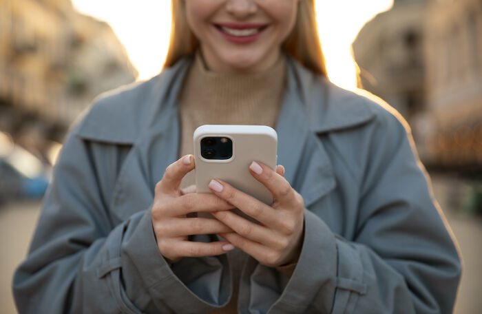 Person in a gray coat smiling at a phone.