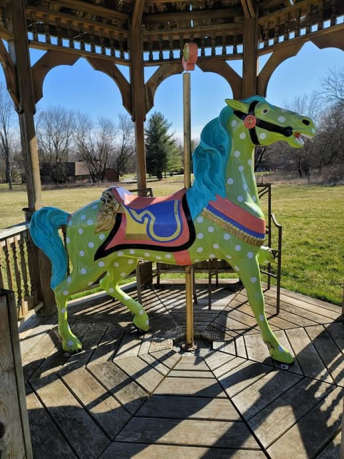 Colorful second-hand carousel horse with dots and blue mane in a wooden gazebo.