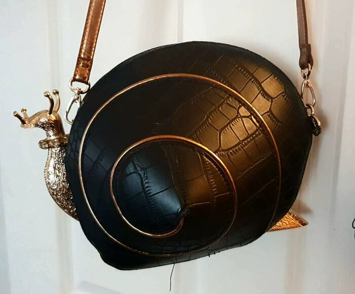 A strange and spectacular snail-shaped handbag with a gold metallic shell detail, hanging on display.