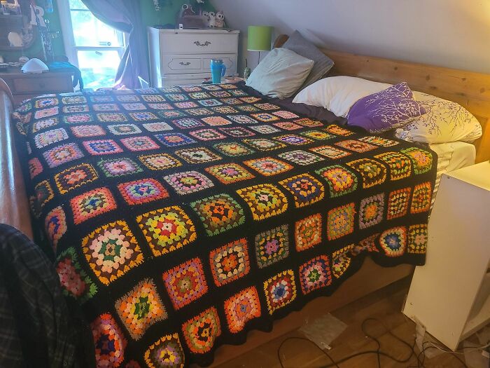 Colorful, second-hand crocheted blanket with intricate patterns covers a bed in a cozy room setting.