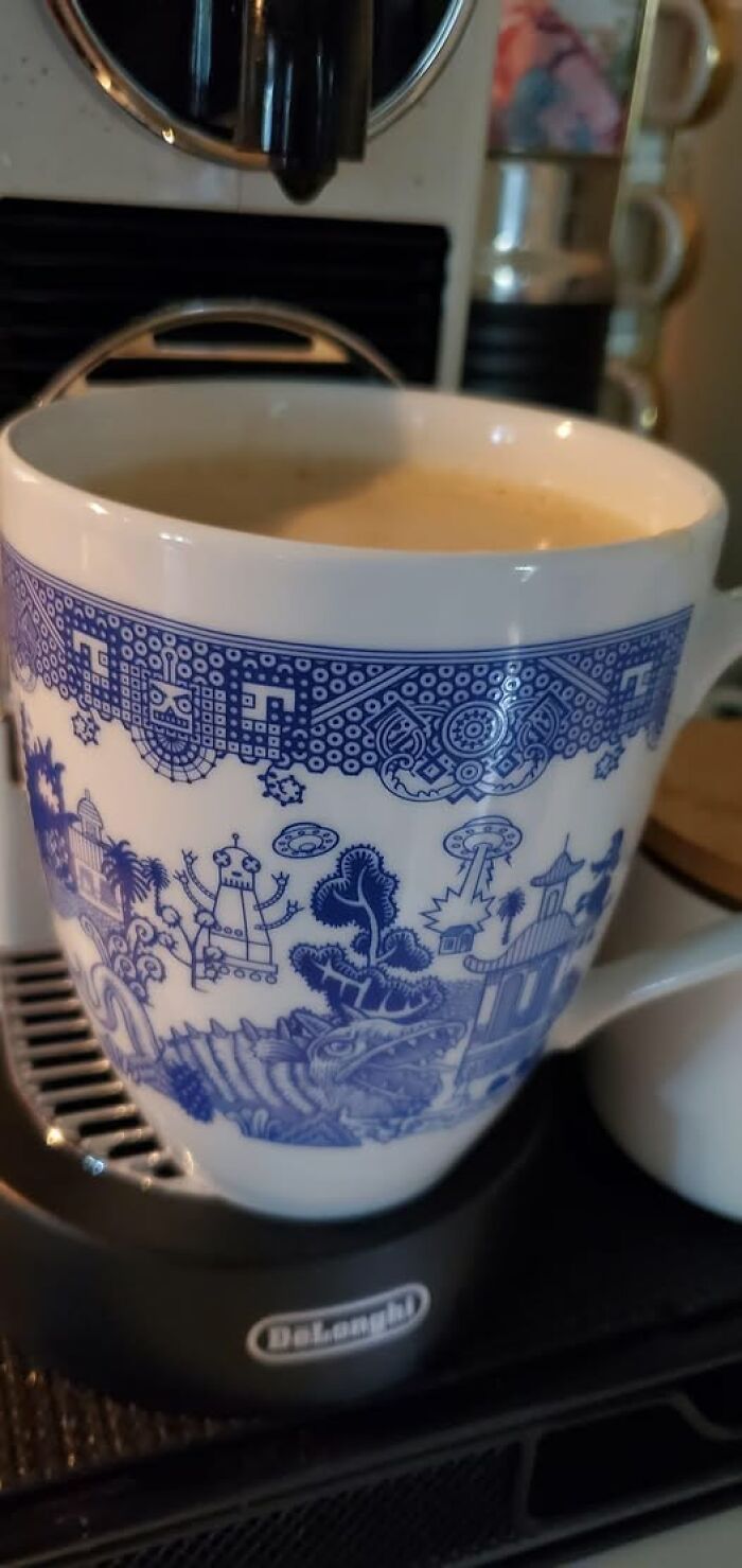 Second-hand mug with an intricate blue design featuring robots and spaceships, on a coffee machine.