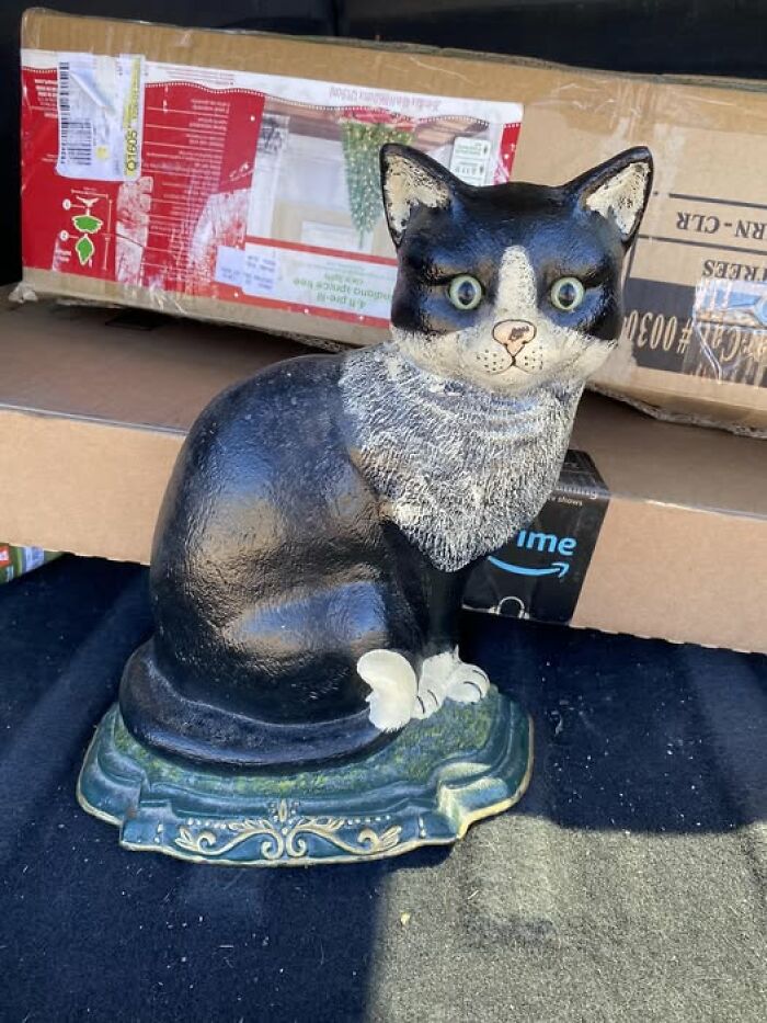 A strange and spectacular second-hand ceramic cat statue with wide eyes, sitting on a decorative base.