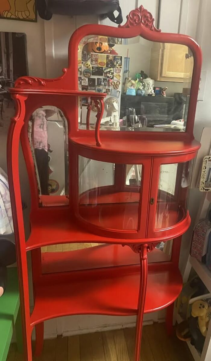 Red vintage cabinet with ornamental design, reflecting its surroundings in a mirror.