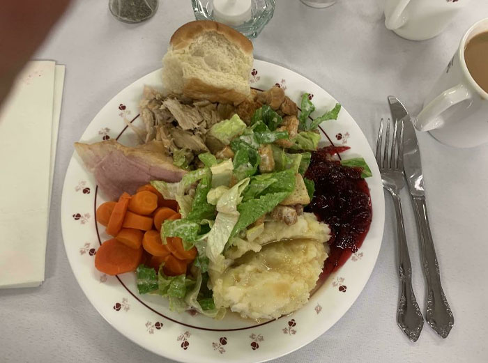 Plate of wholesome Christmas food with turkey, salad, carrots, cranberry sauce, and bread, set on a festive table.