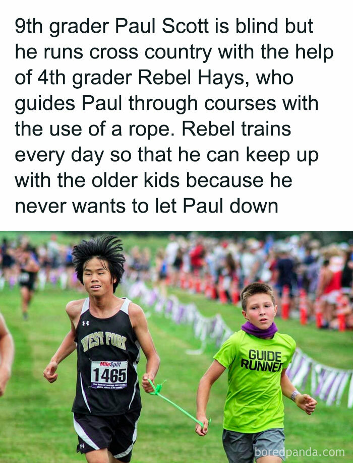 Two boys running in a cross country race, showcasing wholesome-kindness, one guiding the other with a rope.