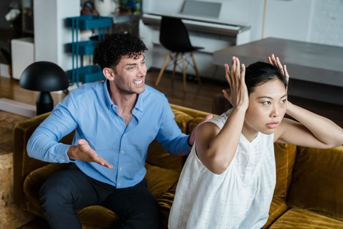 Man looking frustrated and woman looking annoyed during an argument in their living room, highlighting marriage tension.