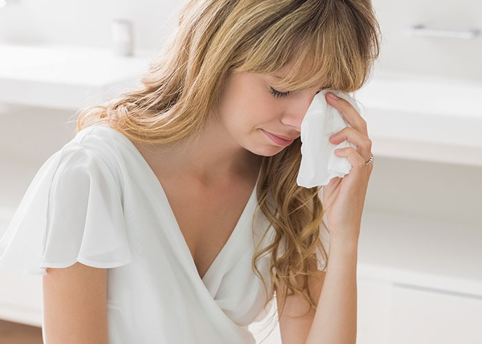 Woman in wedding dress crying, holding tissue in a bathroom.