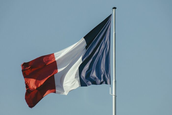 French flag waving on a flagpole against a clear sky.