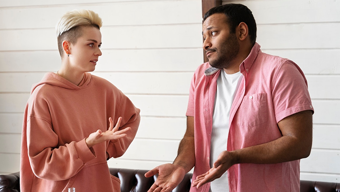 Two friends debating travel plans; one wearing a pink shirt, the other a pink hoodie, in a casual setting.