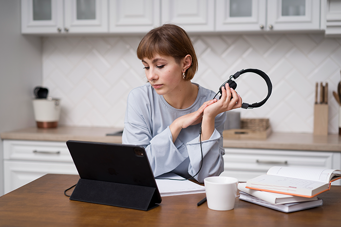 Person planning a Japan trip on a tablet, holding headphones, sitting at a desk in a kitchen setting.