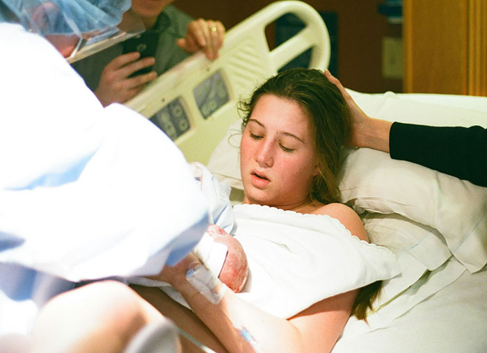 A woman in a hospital bed holding a newborn, surrounded by medical staff, illustrating an insurance claim situation.