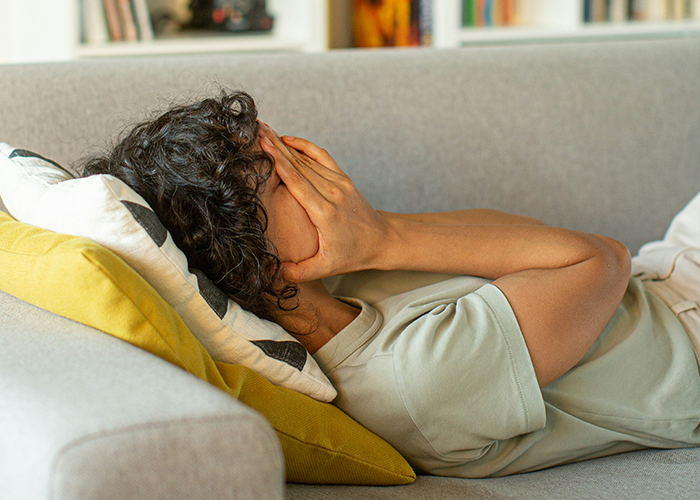 Person lying on a couch, covering face in frustration, illustrating relationship stress from toxic family boundaries.