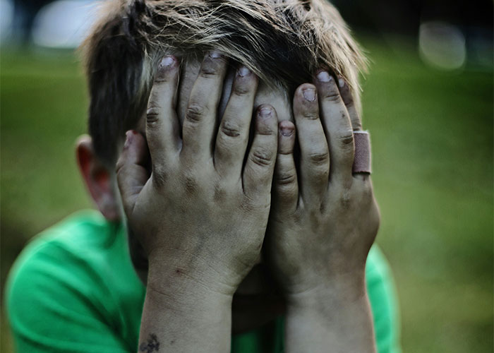 Child in distress with hands over face, green shirt, showing emotional struggle.