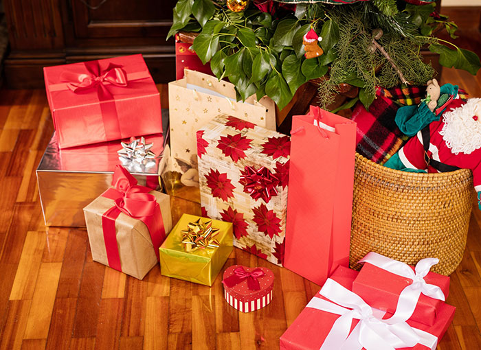 Christmas gifts with colorful wrapping under a decorated tree on a wooden floor.