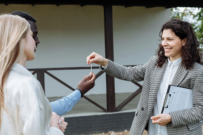 Woman handing keys in a cheerful outdoor setting, with an expression of joy and connection.