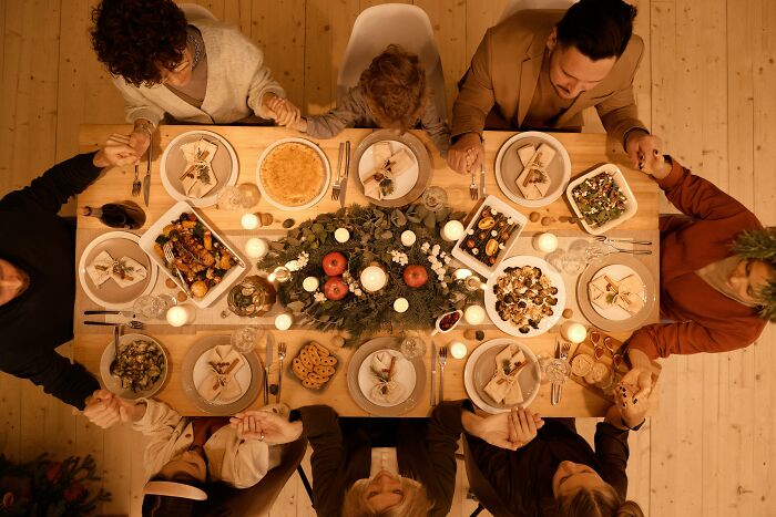 Family holding hands around a Christmas dinner table, decorated with festive greenery and candles.