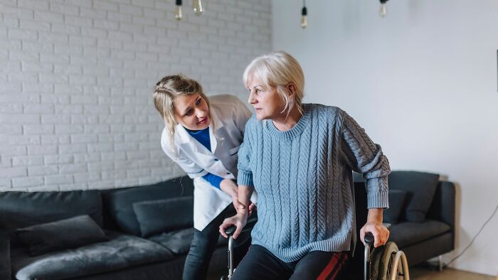 A woman in a wheelchair assisted by a caregiver in a living room, discussing their experience with challenging jobs.